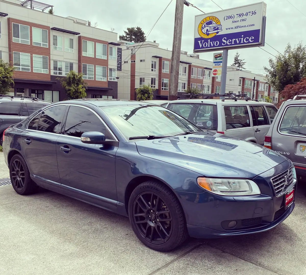 A blue Volvo S80 parked under the All Vovo Volvo Service sign