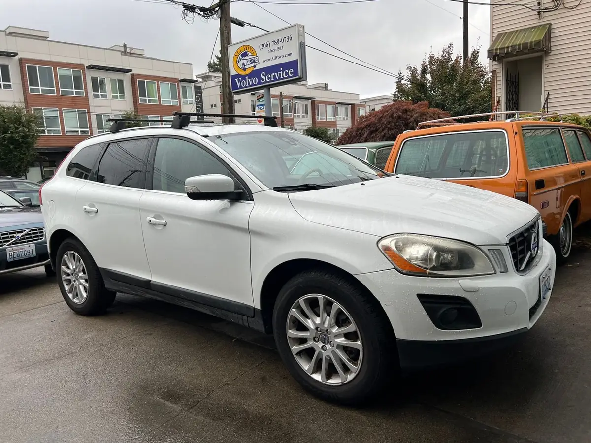 An orange vintage Volvo wagon parked beside a white XC60 under the All Vovo sign