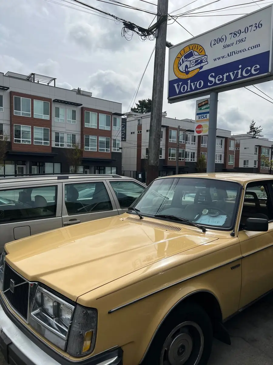 A yellow Volvo 240 under the All Vovo sign